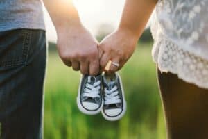 woman and man holding black crib shoes standing near green grass during daytime