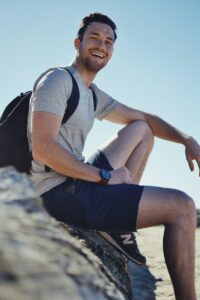 smiling man sitting on gray rock at daytime