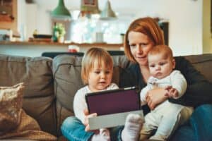 two babies and woman sitting on sofa while holding baby and watching on tablet